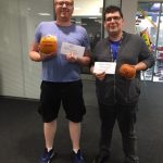 2 men holding what looks like pumpkins and a note