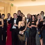 A group of people. most are laughing at looking at different cameras